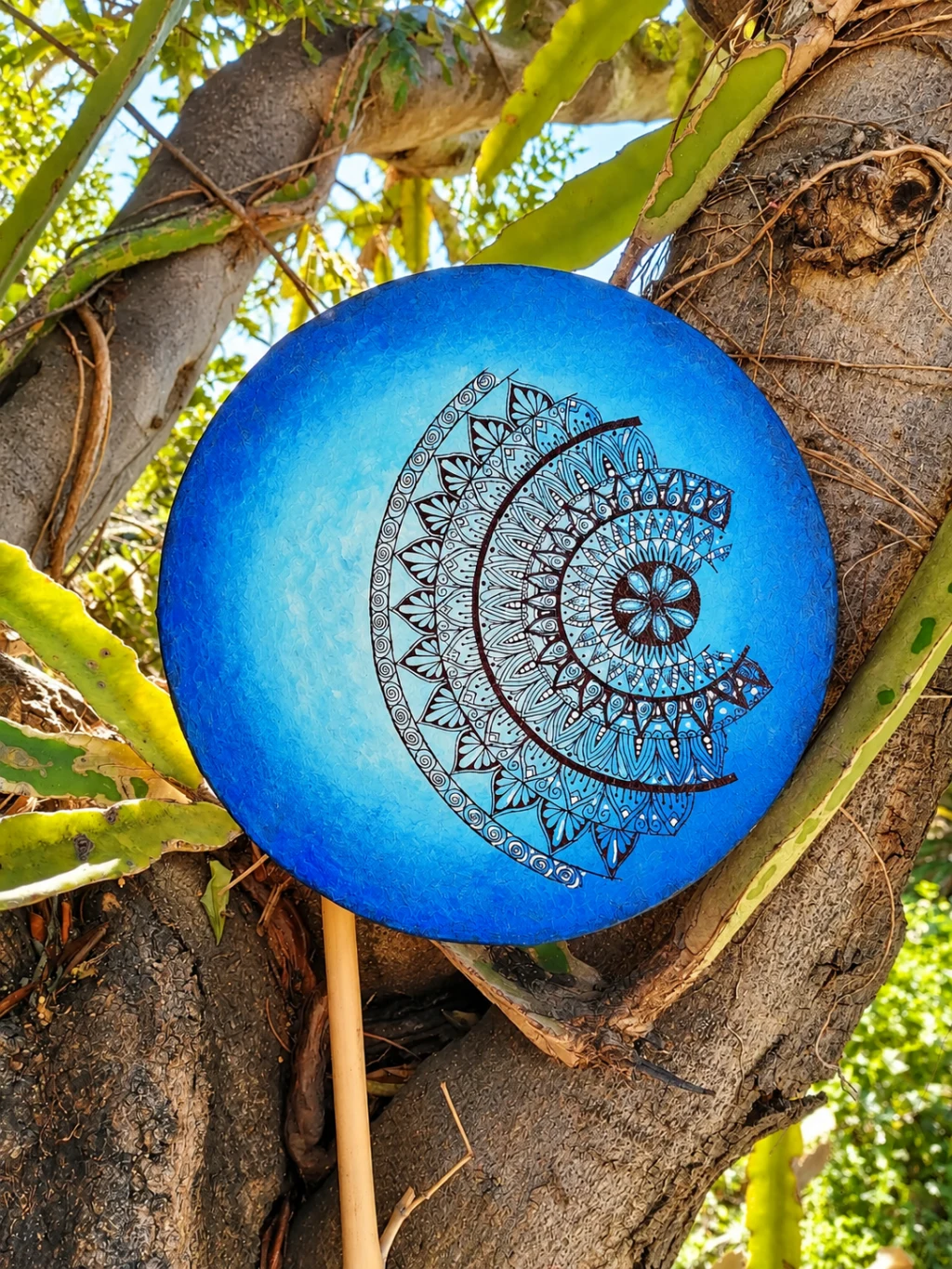 Obra circular azul con un mandala de líneas oscuras fotografiada entre ramas